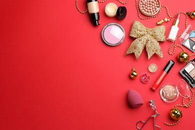 Flat lay composition with makeup products and Christmas decor on red background. Space for text