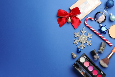 Photo of Flat lay composition with makeup products and Christmas decor on blue background. Space for text