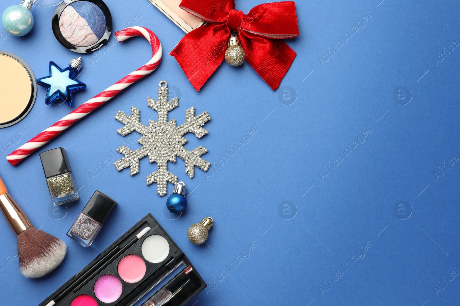 Photo of Flat lay composition with makeup products and Christmas decor on blue background. Space for text