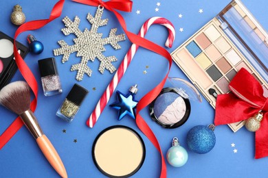 Photo of Flat lay composition with makeup products and Christmas decor on blue background