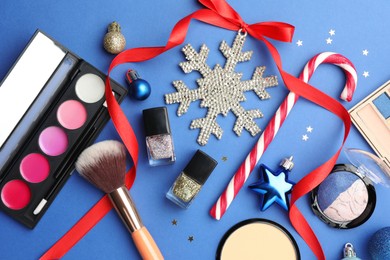 Photo of Flat lay composition with makeup products and Christmas decor on blue background