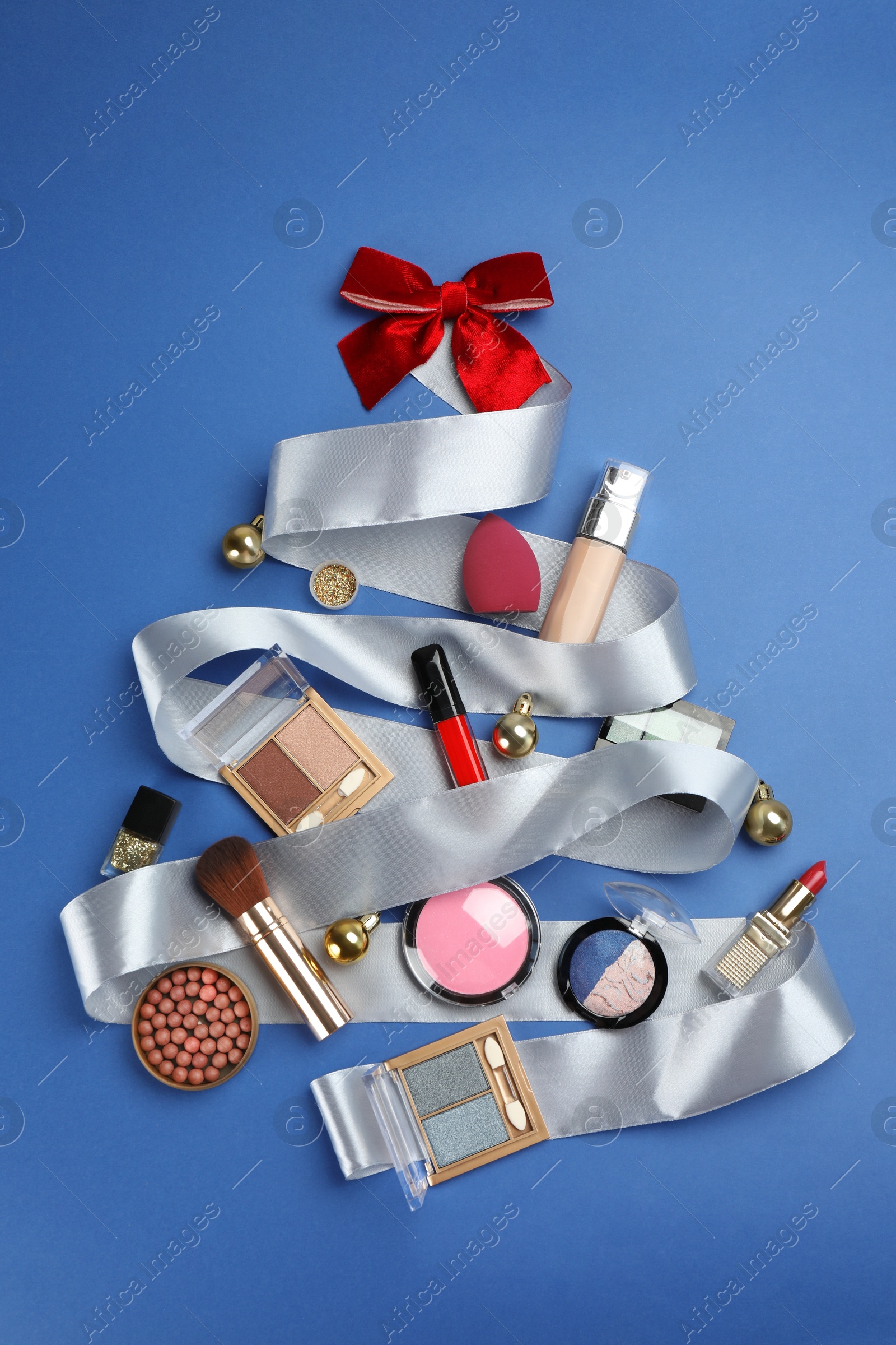 Photo of Christmas tree made of decorative cosmetic products and festive decor on blue background