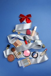 Photo of Christmas tree made of decorative cosmetic products and festive decor on blue background