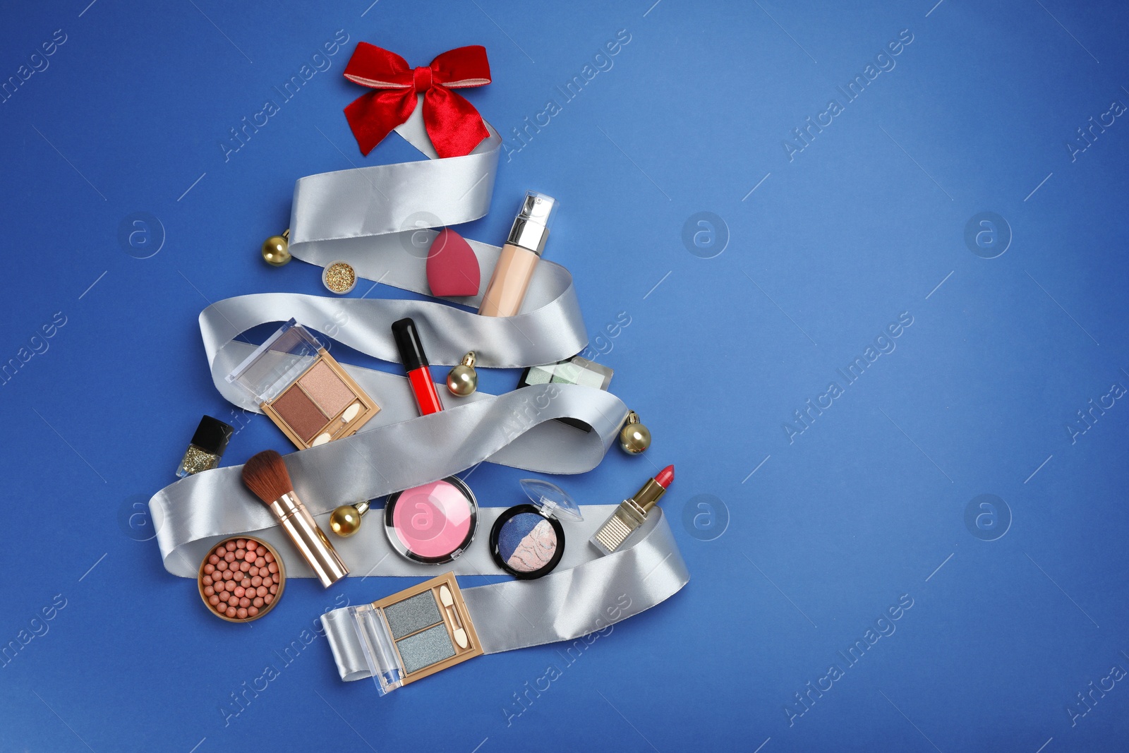 Photo of Christmas tree made of decorative cosmetic products and festive decor on blue background. Space for text