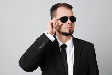 Young bodyguard in suit and sunglasses on grey background