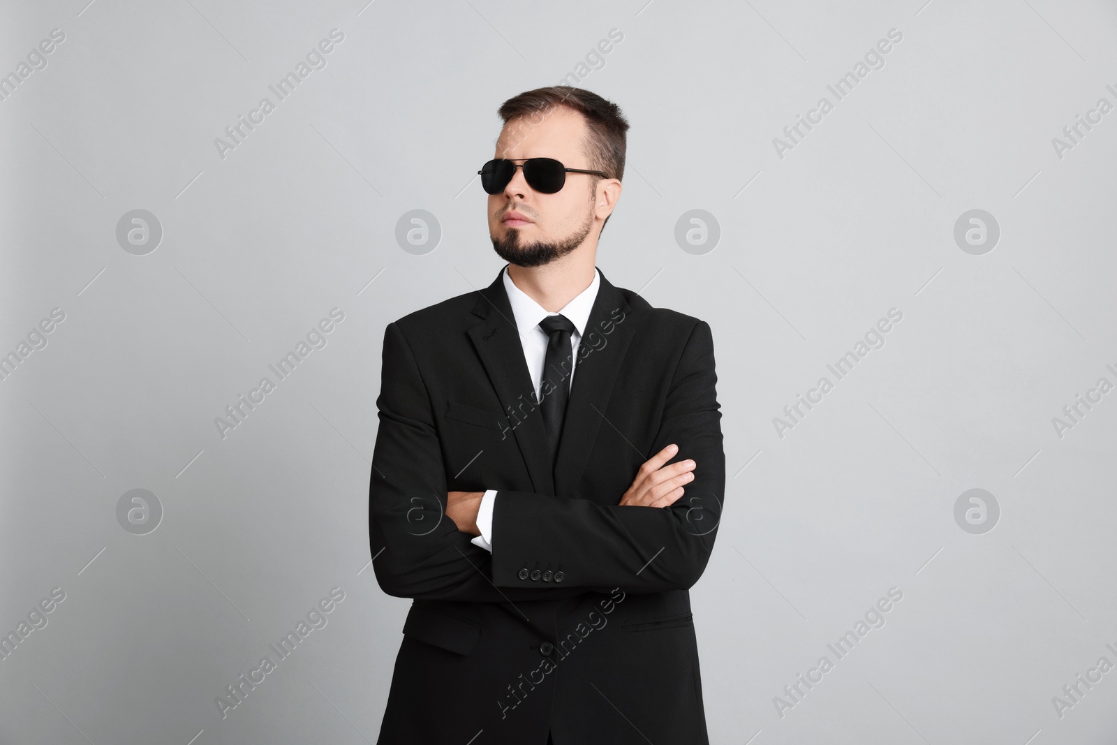 Photo of Young bodyguard in suit and sunglasses on grey background