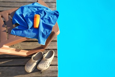 Stylish beach slippers, towel and sunscreen on wooden deck near outdoor swimming pool, top view