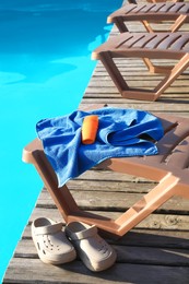 Stylish beach slippers, towel and sunscreen near outdoor swimming pool