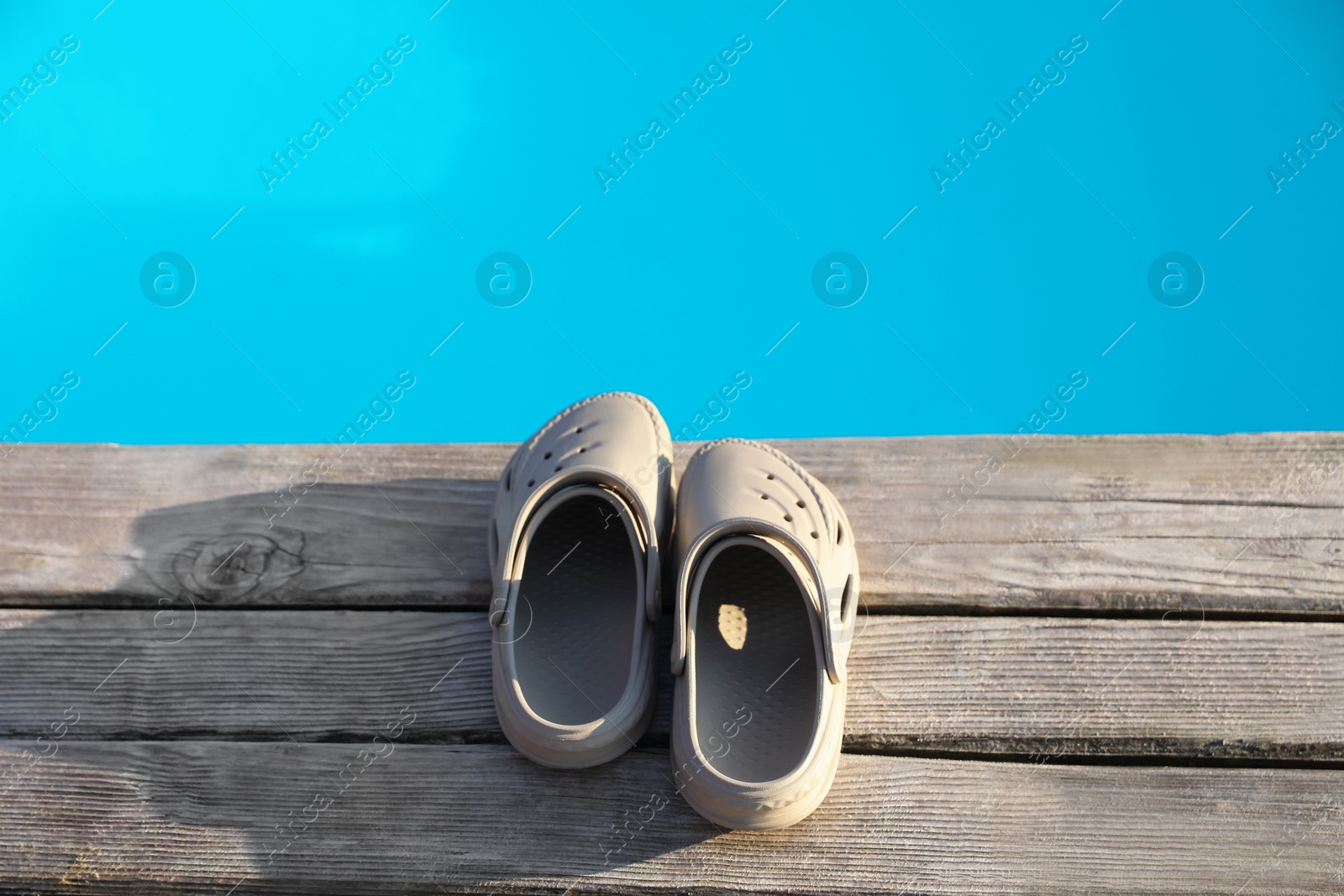 Photo of Stylish beach slippers on wooden deck near outdoor swimming pool