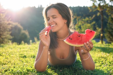 Happy woman eating juicy watermelon on green grass outdoors, space for text