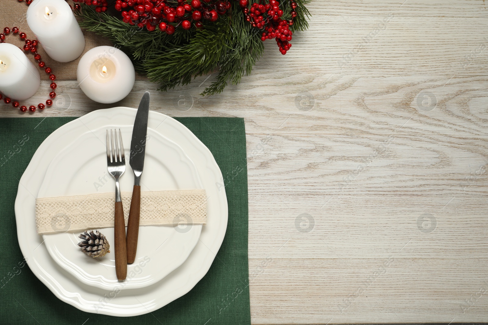 Photo of Christmas place setting with plates, cutlery and festive decor on wooden table, flat lay. Space for text