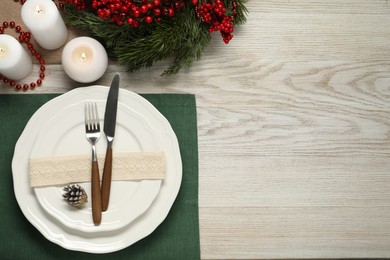 Photo of Christmas place setting with plates, cutlery and festive decor on wooden table, flat lay. Space for text