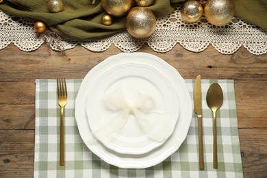 Photo of Christmas place setting with plates, cutlery and festive decor on wooden table, flat lay