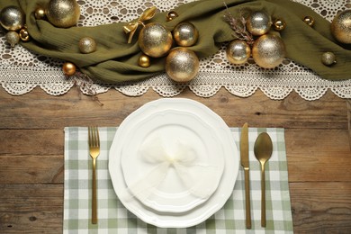 Photo of Christmas place setting with plates, cutlery and festive decor on wooden table, flat lay