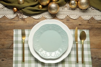 Photo of Christmas place setting with plates, cutlery and festive decor on wooden table, flat lay