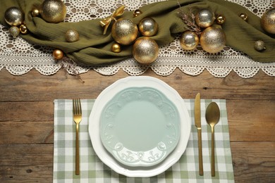 Photo of Christmas place setting with plates, cutlery and festive decor on wooden table, flat lay