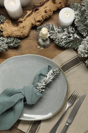 Photo of Christmas place setting with plate, cutlery and festive decor on wooden table, flat lay