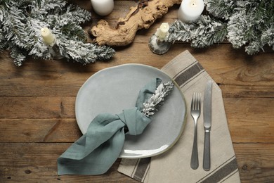 Photo of Christmas place setting with plate, cutlery and festive decor on wooden table, flat lay