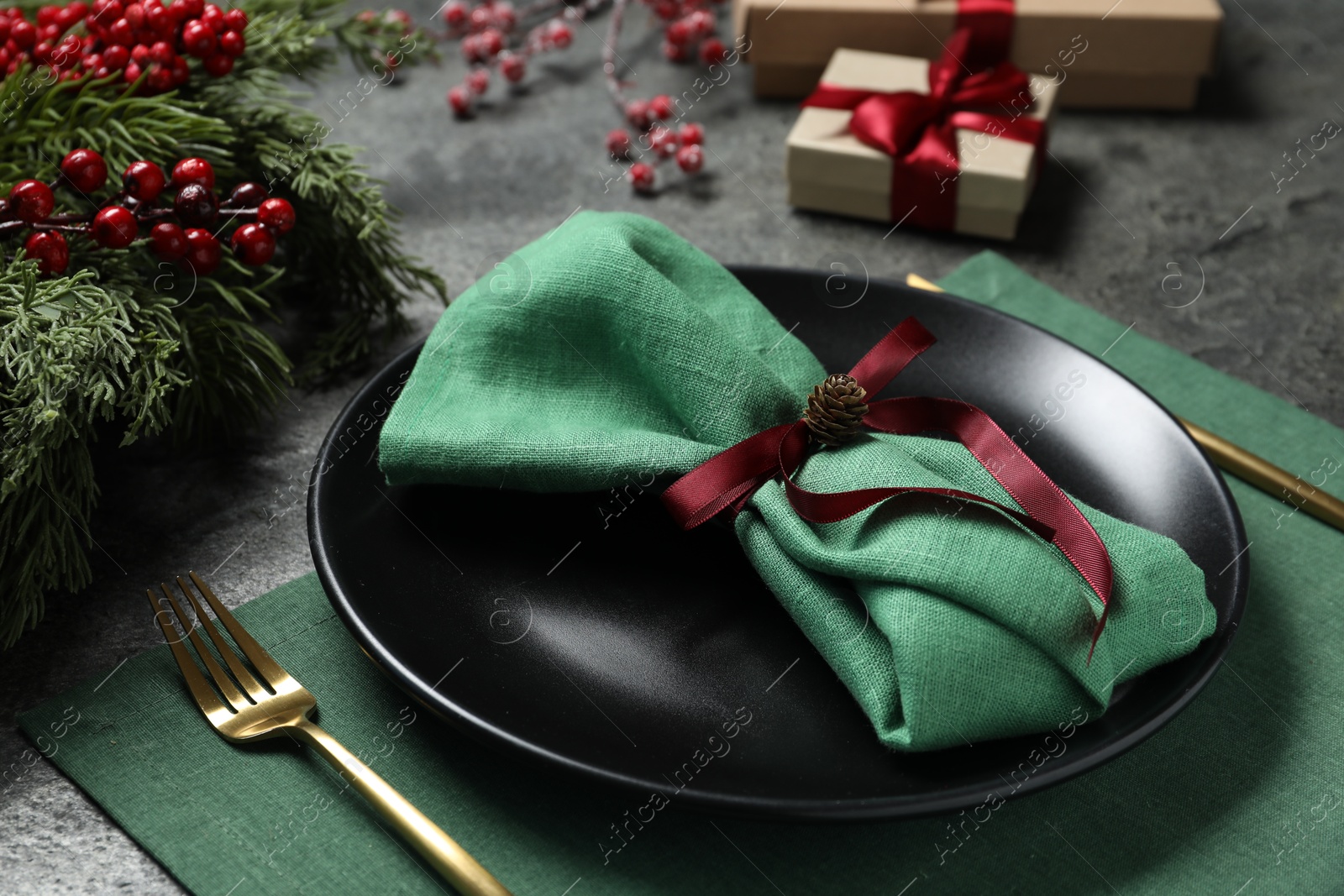 Photo of Plate, fork, napkin and Christmas decor on grey table, closeup