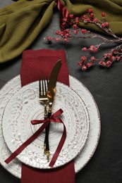 Photo of Christmas place setting with plates, cutlery and festive decor on black table, flat lay