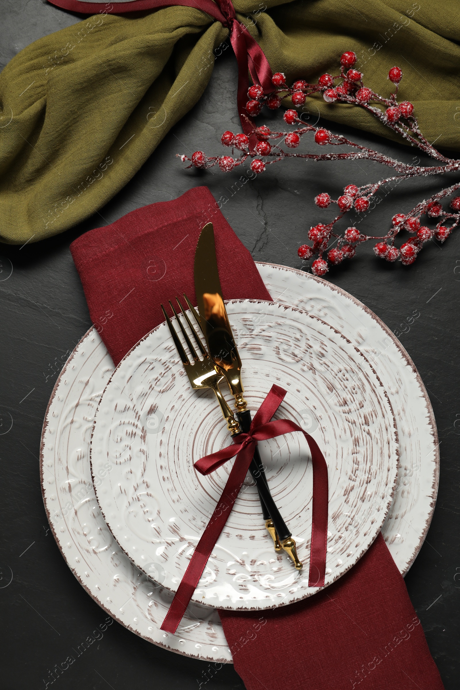 Photo of Christmas place setting with plates, cutlery and festive decor on black table, flat lay