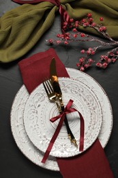 Photo of Christmas place setting with plates, cutlery and festive decor on black table, flat lay