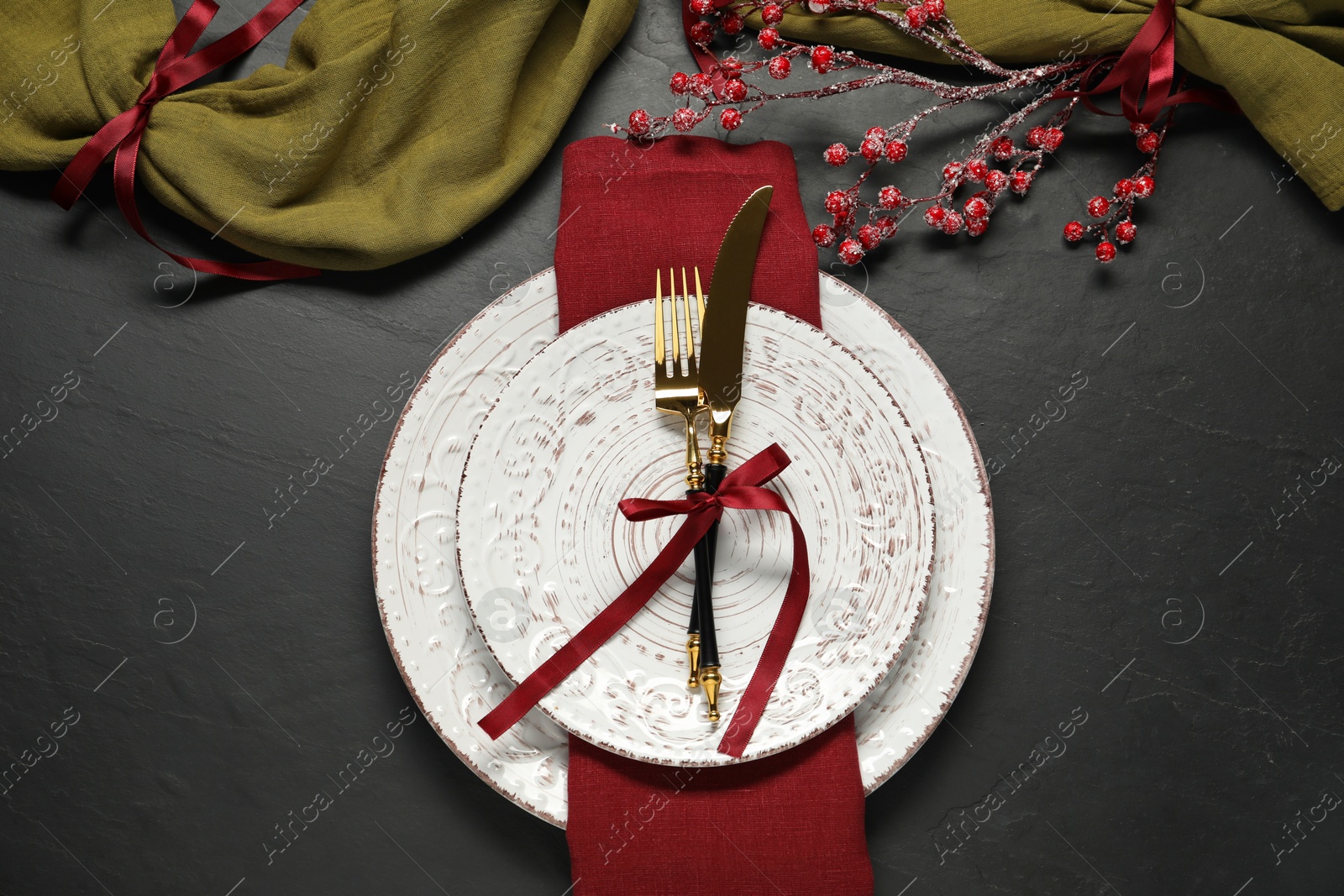 Photo of Christmas place setting with plates, cutlery and festive decor on black table, flat lay