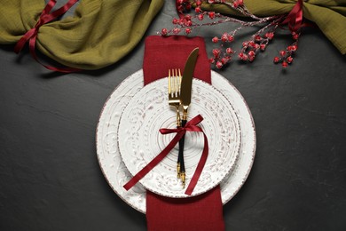 Photo of Christmas place setting with plates, cutlery and festive decor on black table, flat lay