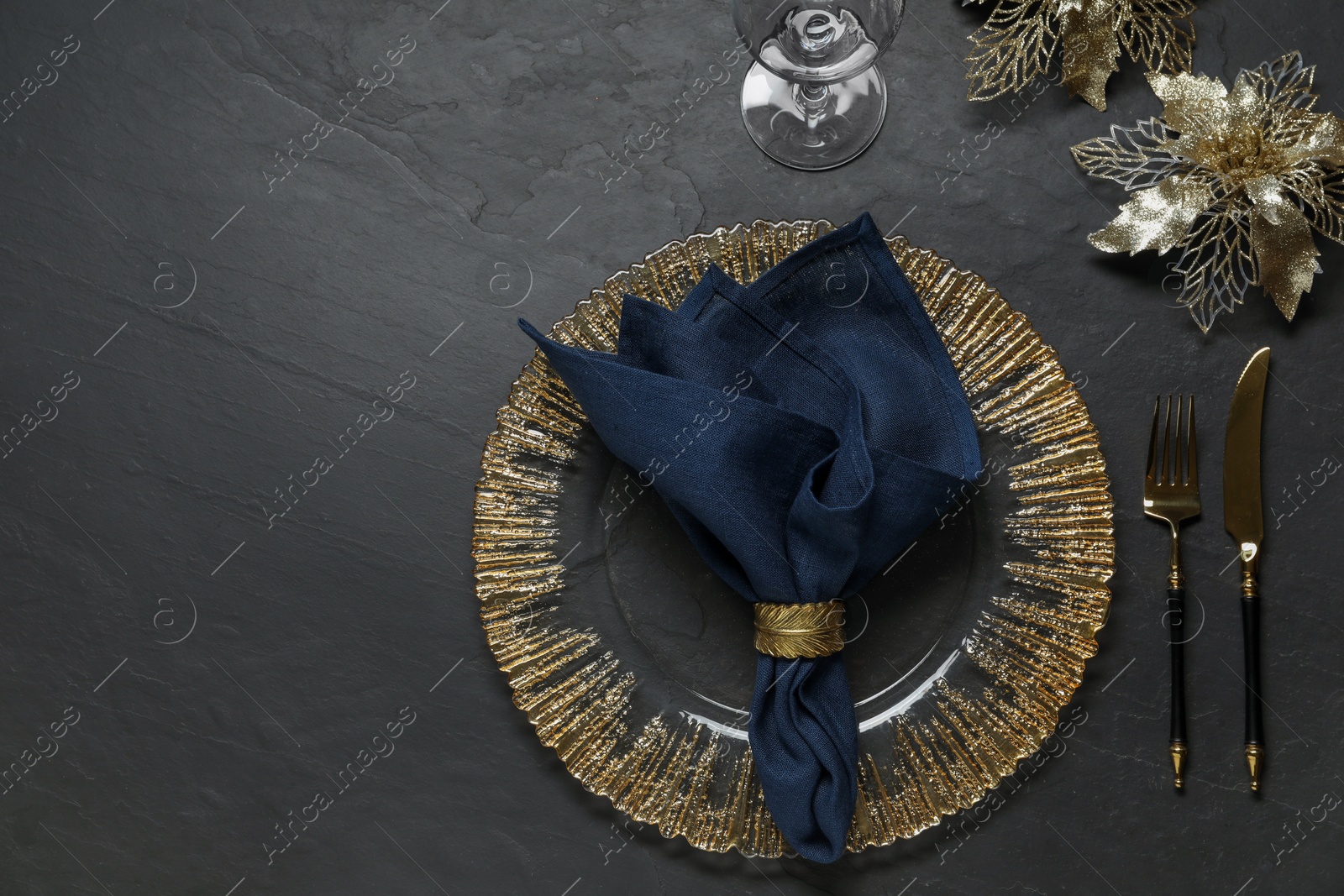 Photo of Christmas place setting with plate, cutlery, glass and festive decor on black table, flat lay. Space for text