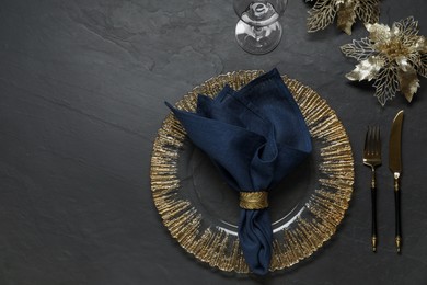 Photo of Christmas place setting with plate, cutlery, glass and festive decor on black table, flat lay. Space for text