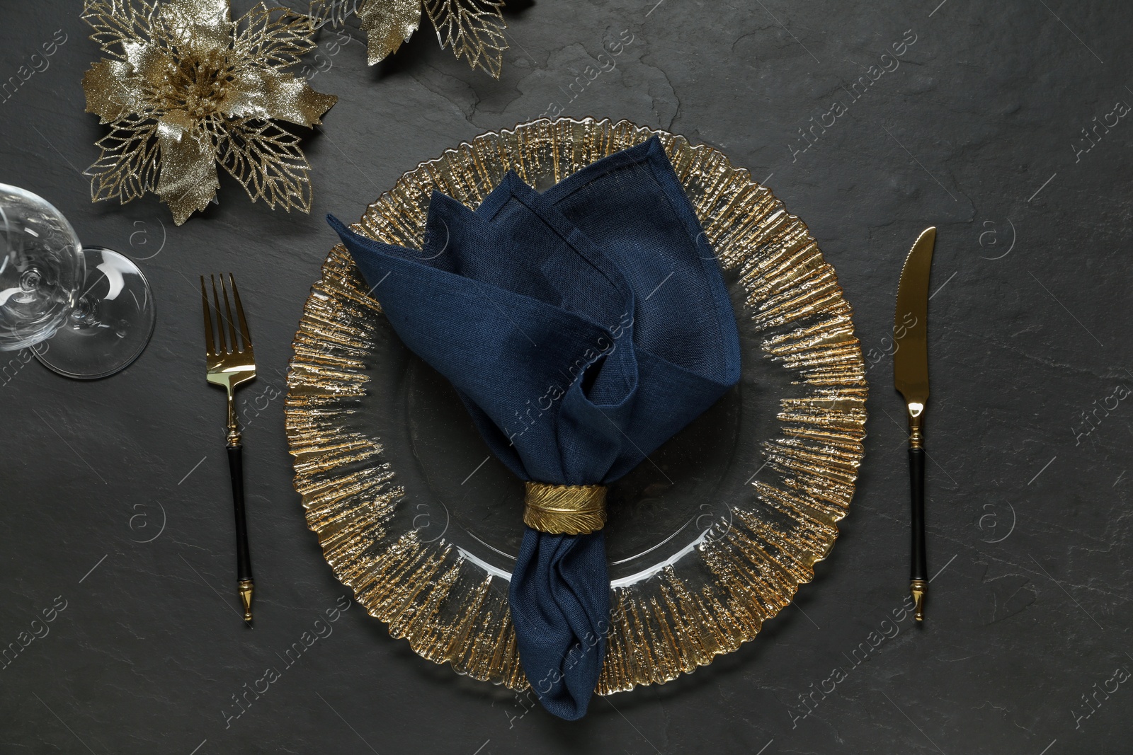 Photo of Christmas place setting with plate, cutlery, glass and festive decor on black table, flat lay