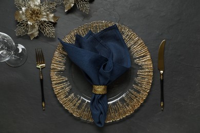 Photo of Christmas place setting with plate, cutlery, glass and festive decor on black table, flat lay