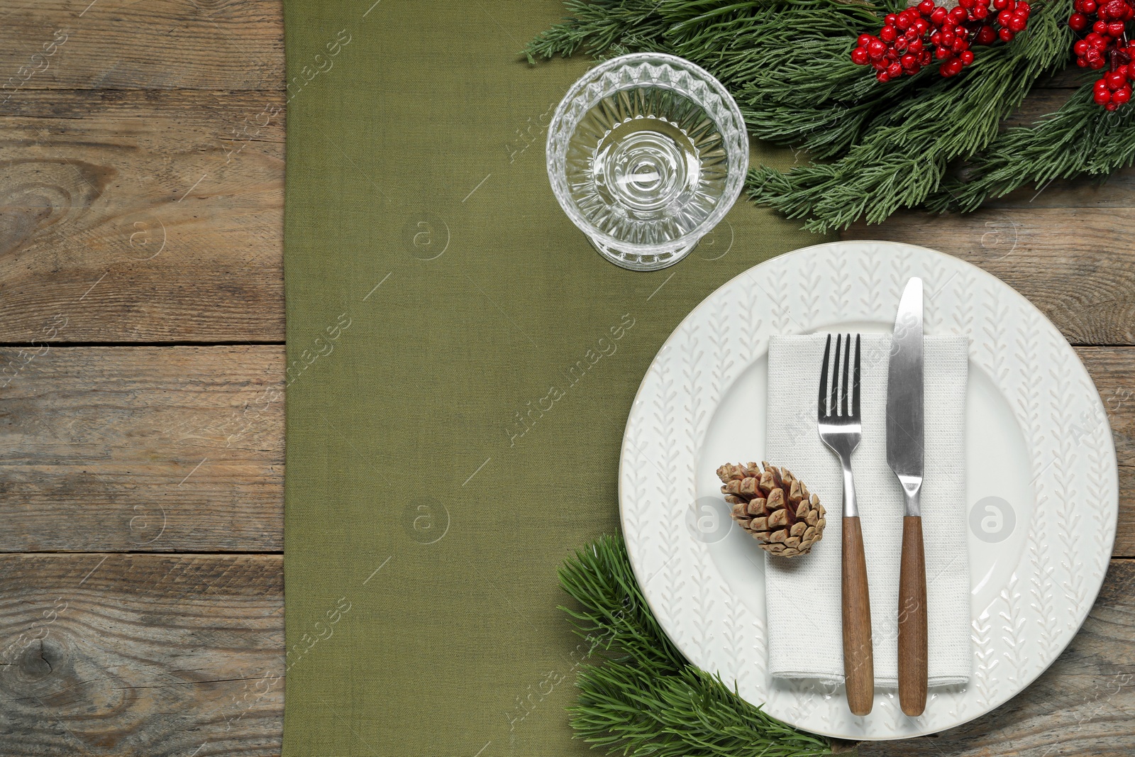 Photo of Christmas place setting with plate, cutlery, glass and festive decor on wooden table, flat lay