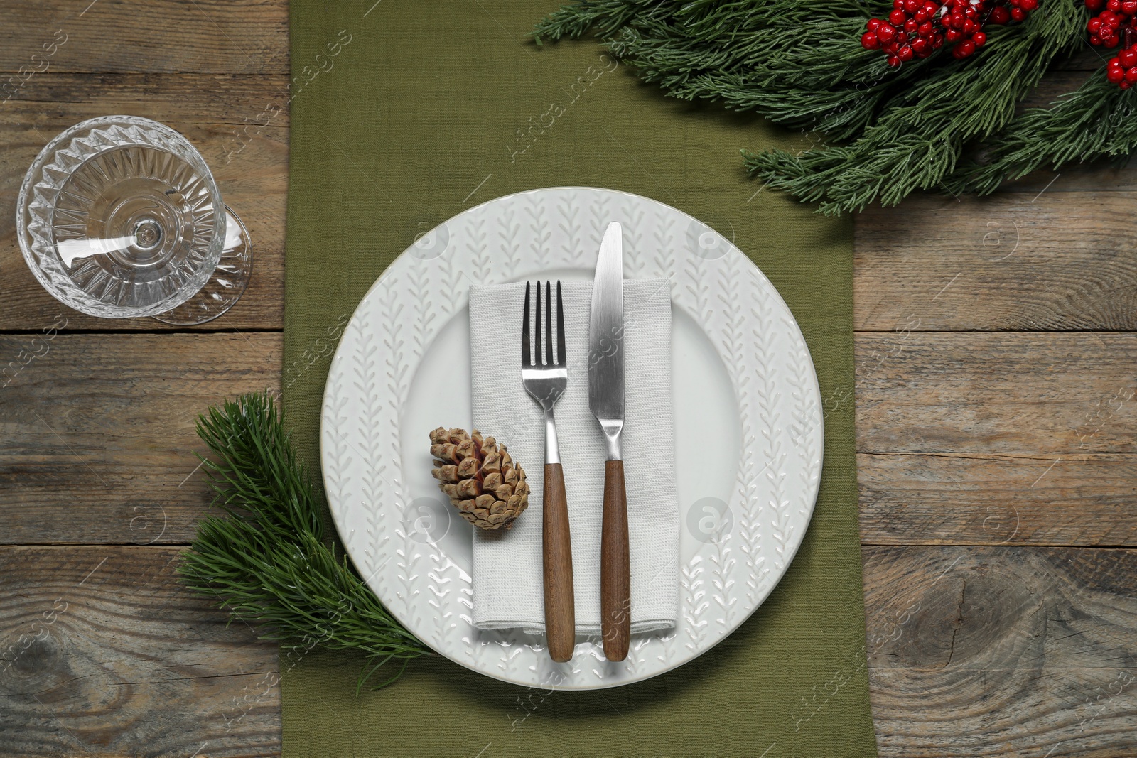 Photo of Christmas place setting with plate, cutlery, glass and festive decor on wooden table, flat lay