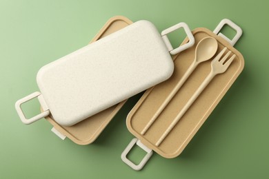 Photo of Compartments of plastic lunch box with cutlery on green background, flat lay