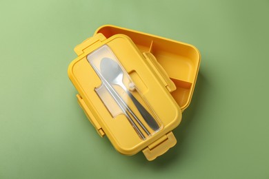 Photo of Empty lunch box with cutlery on green background, top view