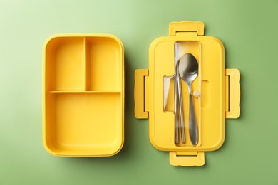 Photo of Empty lunch box with cutlery on green background, top view