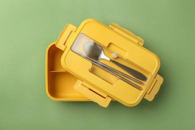 Photo of Empty lunch box with cutlery on green background, top view