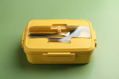 Photo of Yellow lunch box with cutlery on green background