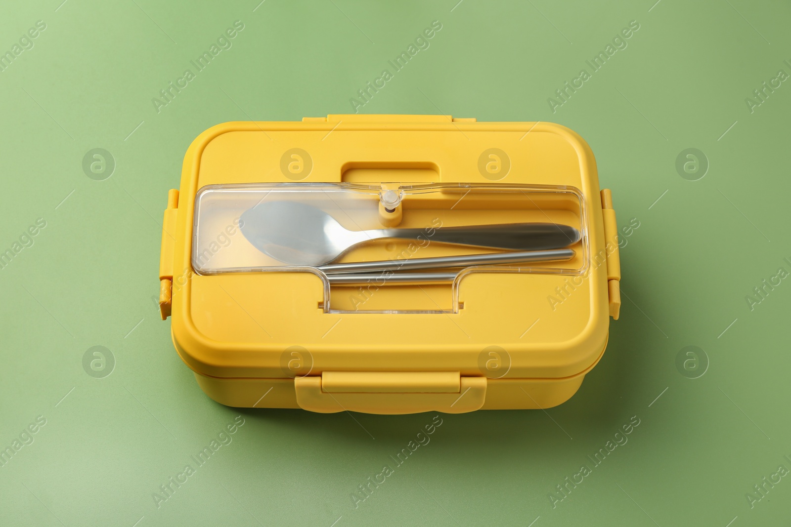 Photo of Yellow lunch box with cutlery on green background