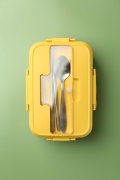 Photo of Yellow lunch box with cutlery on green background, top view