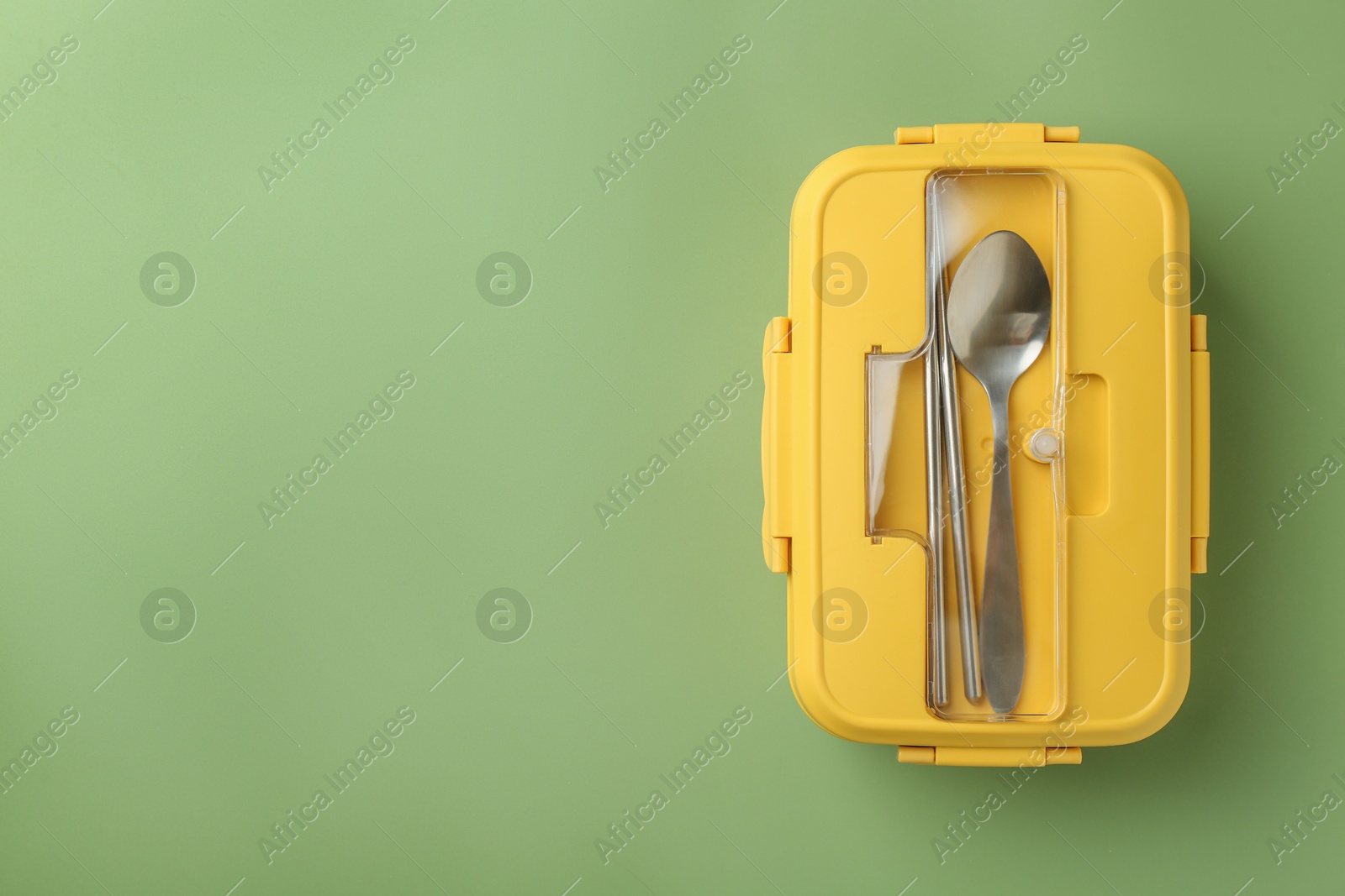 Photo of Yellow lunch box with cutlery on green background, top view. Space for text