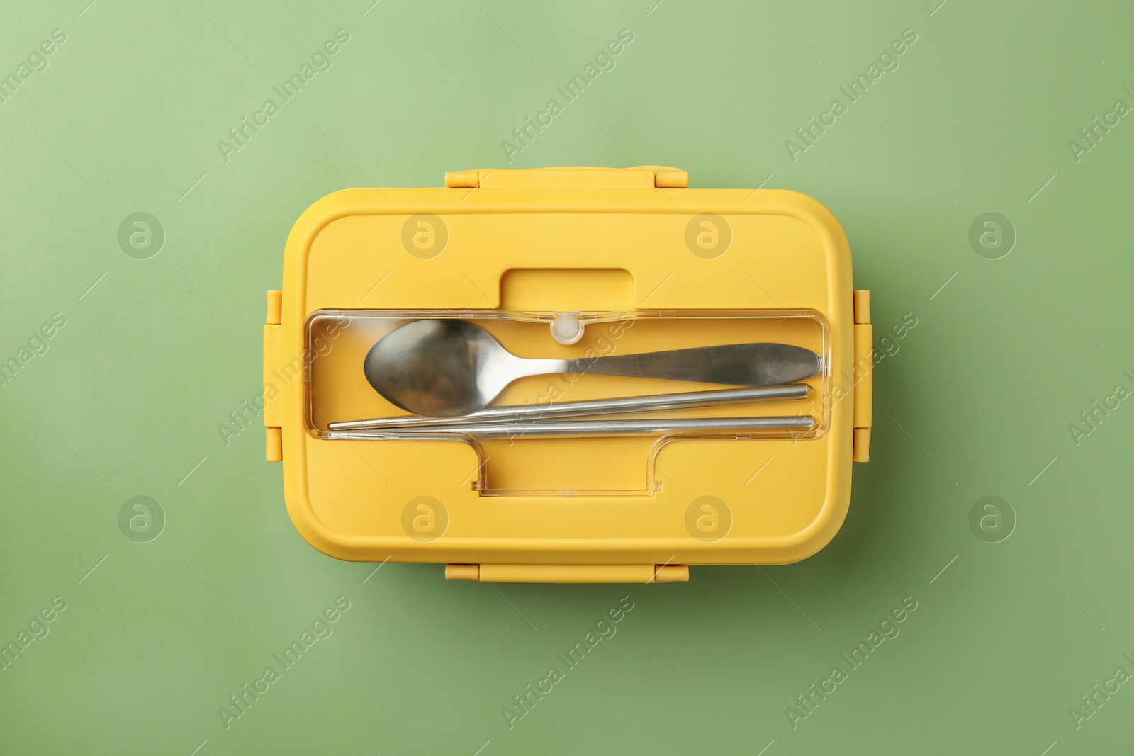 Photo of Yellow lunch box with cutlery on green background, top view