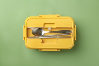 Photo of Yellow lunch box with cutlery on green background, top view