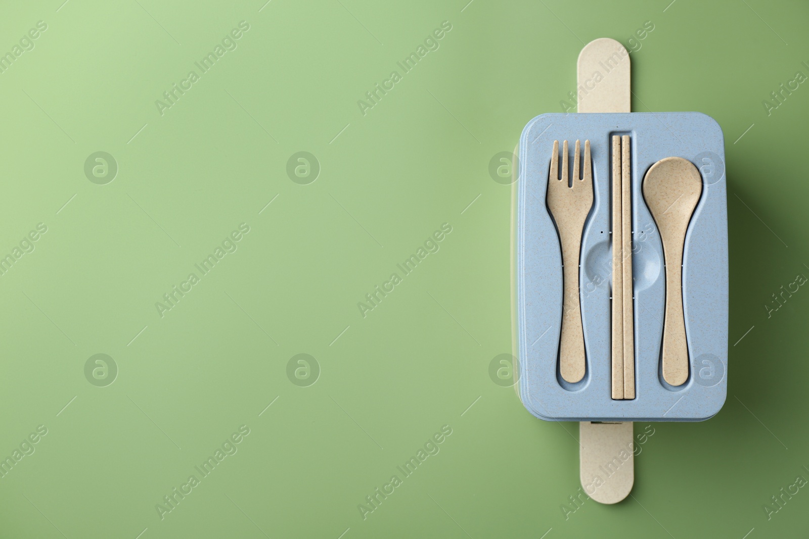 Photo of Lunch box with cutlery on green background, top view. Space for text