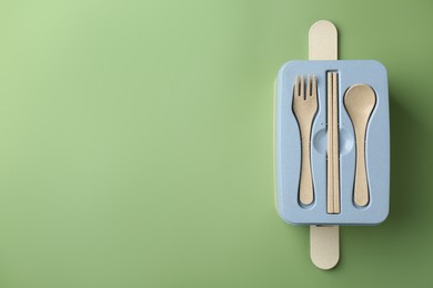 Photo of Lunch box with cutlery on green background, top view. Space for text