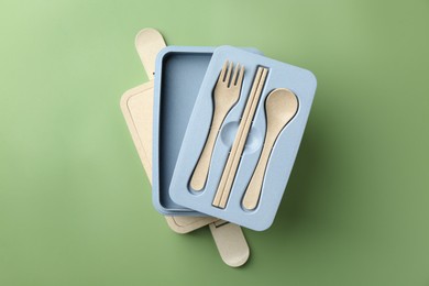 Photo of Empty lunch box with cutlery on green background, top view