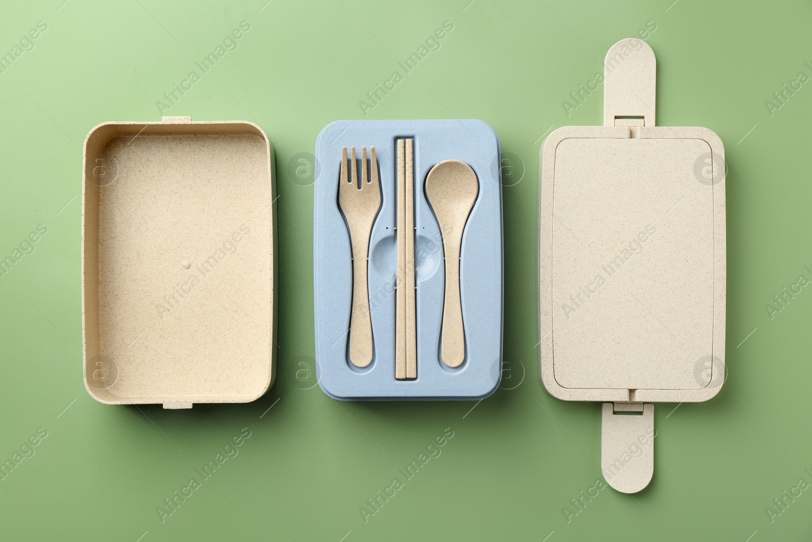 Photo of Plastic lunch box with cutlery and lid on green background, flat lay