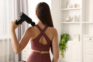 Photo of Woman using percussive massager to relieve trapezius muscle at home, back view. Space for text