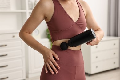 Woman using percussive massager to relieve abdominal muscles at home, closeup